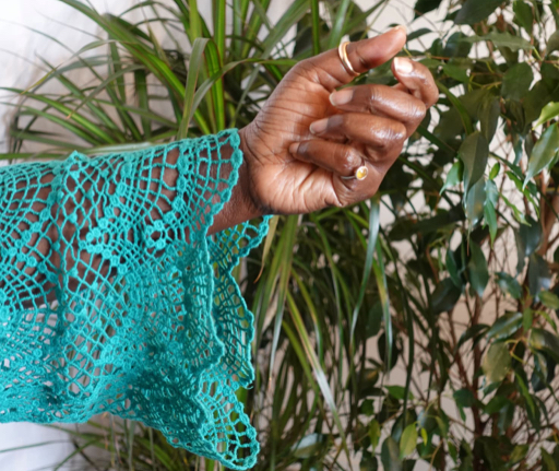 A hand in a teal lace sleeve held gently closed among green leaves