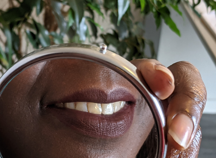 Yolanda's smile reflected in a small round mirror held in her hand, green leaves behind
